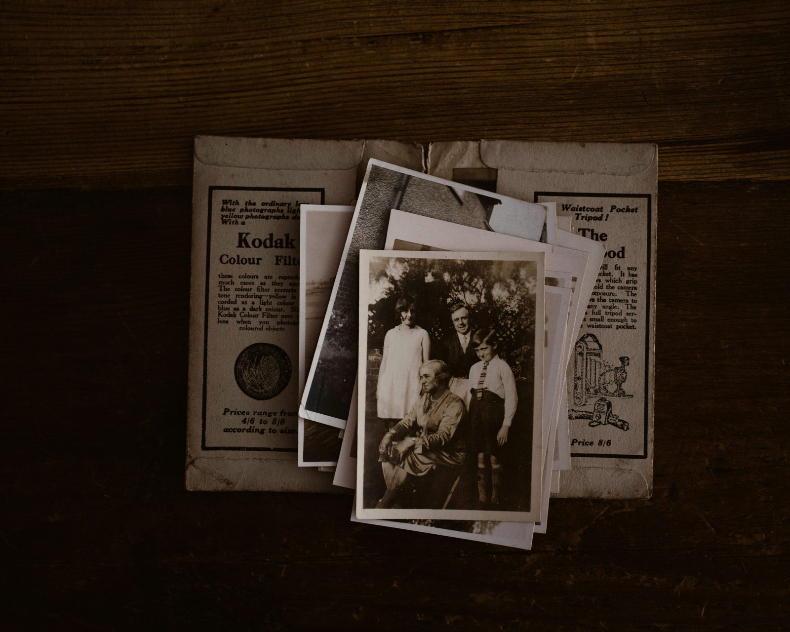Des photographies anciennes sorties d'une pochette Kodak, posées sur une table en bois sombre