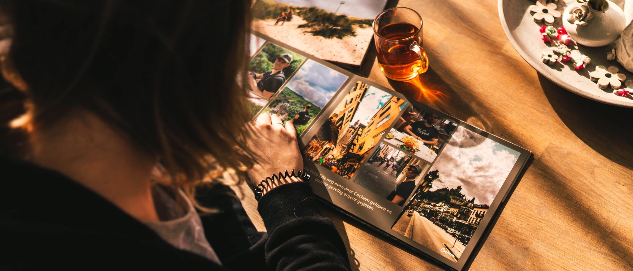 Une femme feuillette un album photo sur une table en bois, dans la lumière du soir